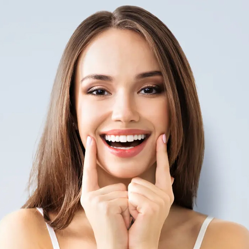 Een lachende vrouw wijst naar haar rechte tanden na een orthodontische behandeling bij Orthodontie Hoogvliet.
