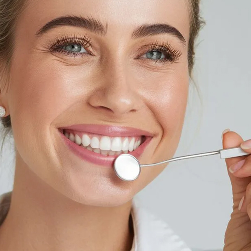 Een glimlachende vrouw tijdens een controle van haar rechte gebit met een tandartsspiegel bij Orthodontie Hoogvliet.
